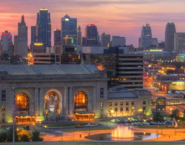 Kansas City skyline at sunset with illuminated buildings and the historic Union Station in the foreground, showcasing a vibrant urban landscape.