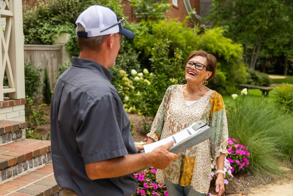 Pest control technician discussing termite inspection details with a smiling homeowner in a garden setting, highlighting customer service and expertise in termite management.